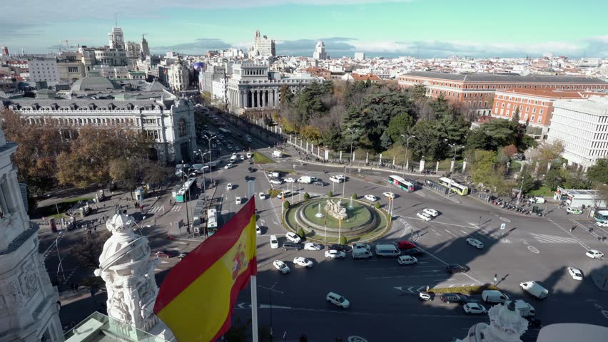 Aerial and panorama view of city rush traffig with spanish flag on the foreground in Cibeles fountain at Plaza de Cibeles. Cibeles Fountain is an iconic place of Madrid City. Spain