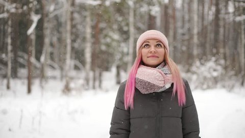 Woman in a jacket and hat in slow motion looks at the snow and catches snowflakes smiling