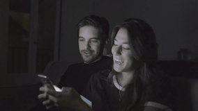 Happy young couple using smartphone at home. Cheerful young man and woman talking and using cell phone together in the evening. Connection concept