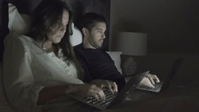 Young couple using laptops in bed. Concentrated young man and woman typing on laptops while lying together in bed. Technology concept