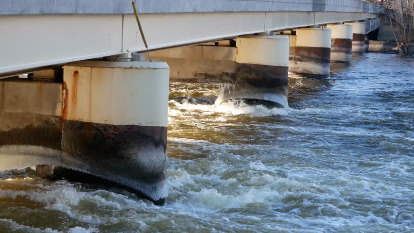 Water flowing under a bridge during the day on the Fox River in Appleton, Wisconsin.
