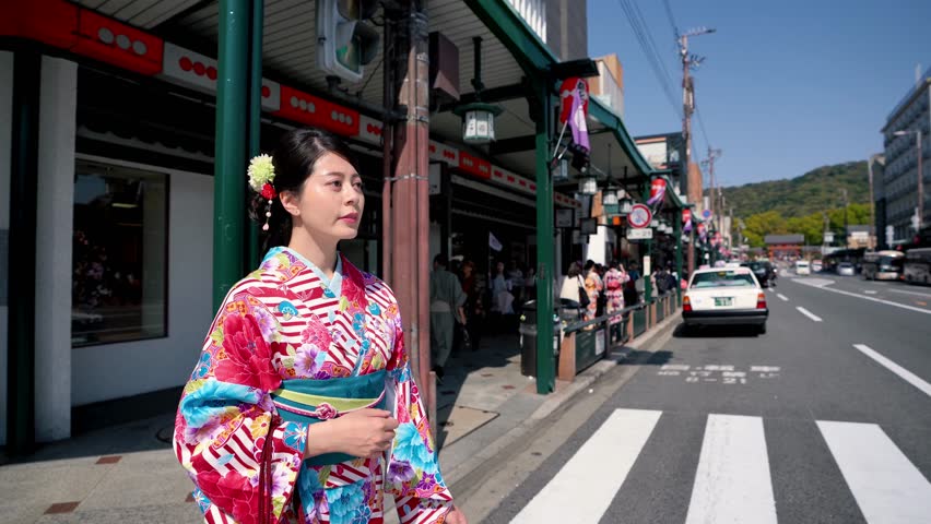 young local japanese lady in floral kimono dress walking on zebra crossing in city urban kyoto japan. tourists following tour guide with flag and high school students on the road on sunny day.