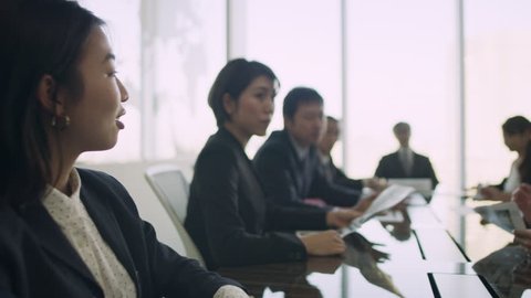 Group of Japanese business people working together around a large table in a conference room with soft natural lighting. Medium shot on 4k RED camera.