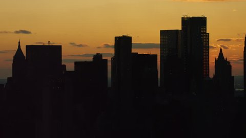 Shot on 4k RED camera on helicopter. Aerial view of silhouettes of buildings and skyscrapers in downtown Manhattan, New York City with soft sunset sky.