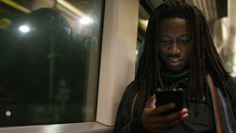 Handsome black man with dreadlocks checking his phone on a train at night