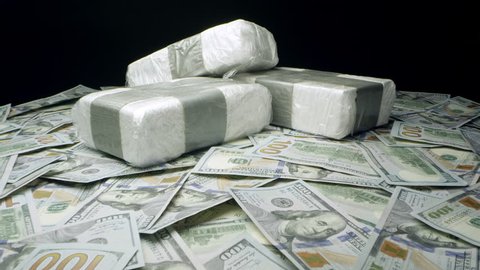 Slow push in towards bricks of drugs on table top of money.
