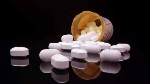 Moving over top of prescription opioid drugs on black table moving in towards bottle on its side.