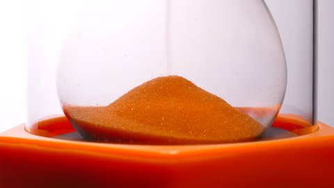Closeup POV shot of a bright orange glass timer in action, with orange sand flowing and forming a moving heap at the bottom. 
