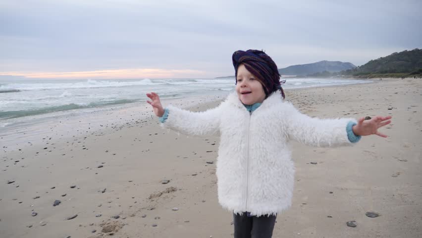 Little cute child girl has fun running slow motion on winter Spanish ocean beach