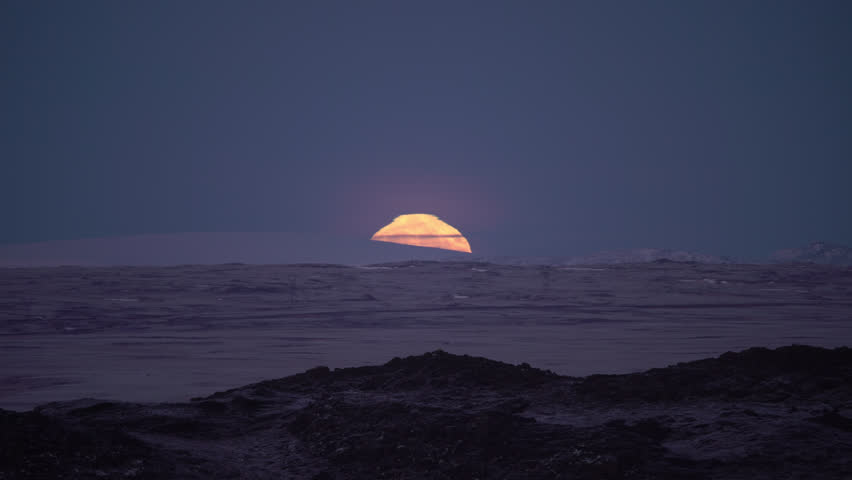 Full moon rising over mountain ridge, power lines and road, Iceland winter.
