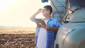 smart farming driver . man farmer driver stands with a digital tablet near the truck. slow motion video. Portrait businessman farmer standing in lifestyle the field harvesting season car. driver