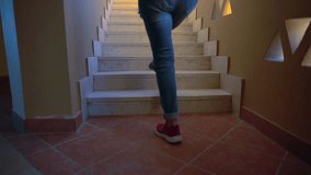 Person walking up a fight of narrow wooden indoor stairs at home in a low angle view of the legs in denim jeans