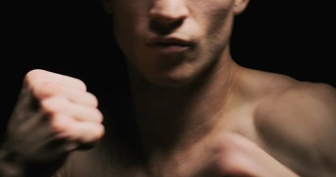 Muscular young man shows the different movements and strikes in the studio on a dark background. Slow motion