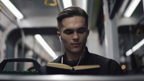 Young handsome man sitting on public transport reading a book - commuter, student, knowledge concept. Young man with headphones in the tram reading a book - Powered by Shutterstock - Get 15% off with code: PIKWIZARD15