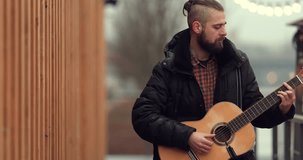 4k Footage of bearded man standing on the street and playing on his guitar with blurred background. - Video