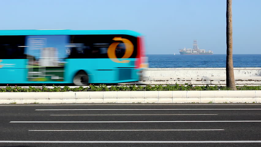Vehicles passing by with cargo ships and oil platforms on the background in Las Palmas, Canary Islands. Traffic on sunny day in the capital of Gran Canaria island, Spain