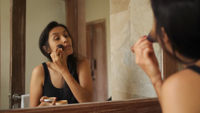 Young Mixed Race Woman Doing Makeup with Brush near Mirror in Hotel Room. 4K. Bali, Indonesia.