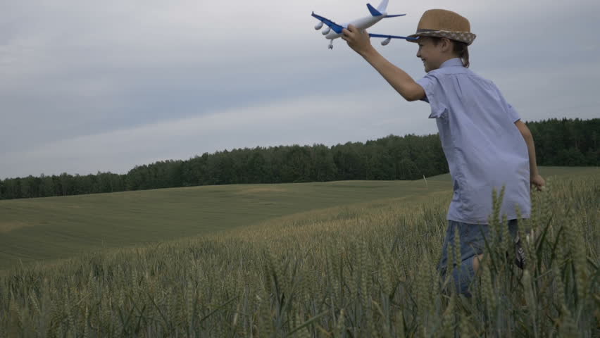 happy boy dreamer with a straw hat runs across the field with an airplane in hand