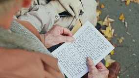 An over the shoulder view of an elderly person opening a handwritten letter in a park with autumn leaves - Powered by Shutterstock - Get 15% off with code: PIKWIZARD15