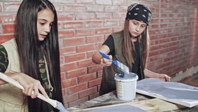Two, happy, young, creative girls dressed as artists, painting in a workshop - slow motion.