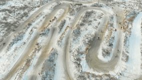 Aerial: Birds eye view of a motocross men riders riding snow track in winter. Winter sports motobike riding. Snow motocross racing aerial video.