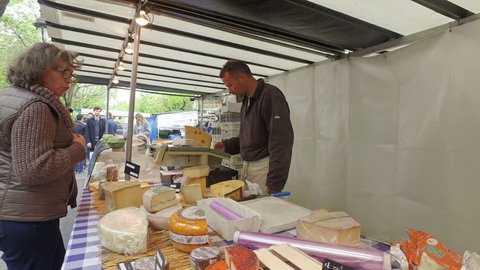 PARIS, FRANCE - circa MAY, 2017: French cheese shop on market near Bastilla in Paris with dozens of kinds of French chees and a worker arranging them