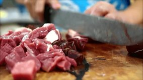 Hand held close up video of raw beef innards being chopped on a chopping board