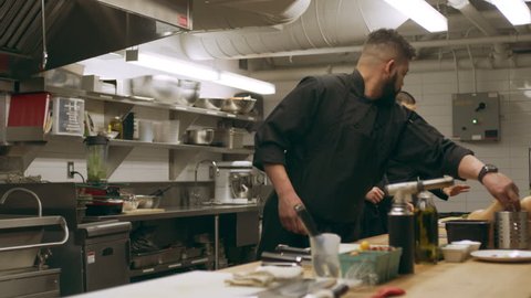 Group of professional chefs setting up at their stations at a long counter in industrial kitchen with soft lighting. Medium shot on 4k RED camera.