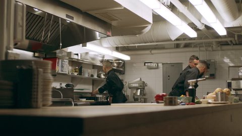 Professional chefs working at their stations at a long counter in industrial kitchen with soft lighting. Medium to close up shot on 4k RED camera on a gimbal.