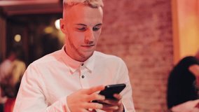 Young Attractive Man Using Smartphone at Evening. He sitting in a bar or restaurant near neon signage. Communication, rest, chatting, travel concept. Close up