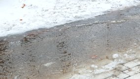 small kid in waterproof rubber boots walking from right to left on puddle of melted snow. closeup 4k outdoor video footage at winter season