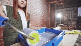 Attractive young girl using a paint roller during house renovation in a close up view on the tray of paint.