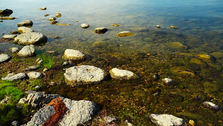 Lake landscape with mountains in the background and rocks in the foreground, on a sunny summer day