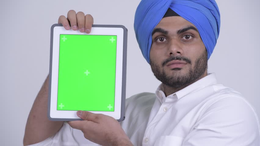 Face of happy young bearded Indian Sikh man showing digital tablet