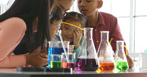 Science teacher teach Asian students in laboratory room, girl uses magnifying glass to look through something, colorful test tube and microscope on table , concept for study in laboratory room.
