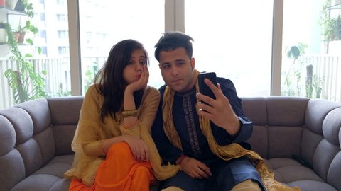Girlfriend and boyfriend take photos dressed in traditional Indian costumes indoor and taking selfies on their camera mobile phone device 