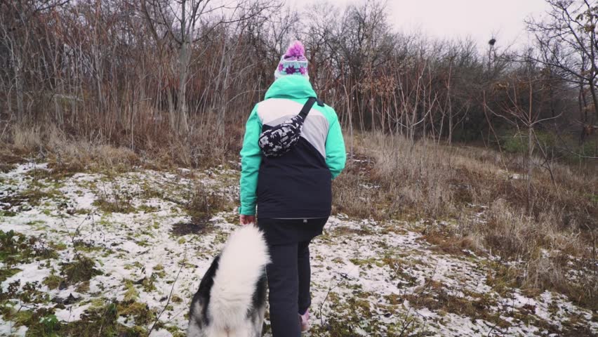 Young beautiful woman walks with her Husky dog at winter around forest. Slow motion