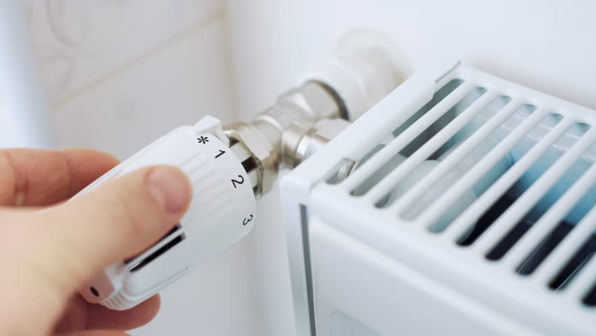 A man regulates the temperature in the house with a thermostat on the radiator. 4K video with shallow depth of field focus. Royalty-Free Stock Footage #1021882939