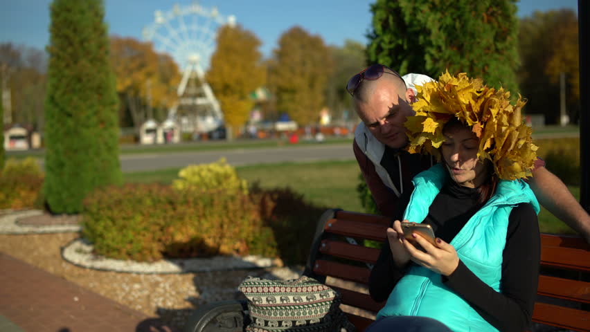 Man and woman in the park on the bench using a smartphone
