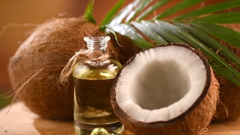 Coconut oil in a bottle with coconuts and green palm tree leaf rotated over brown background. Tropical Coco nut closeup. Healthy Food, skin care concept. Vegan food. 4K UHD video
