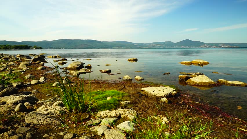 Lake landscape with mountains in the background and rocks in the foreground, on a sunny summer day