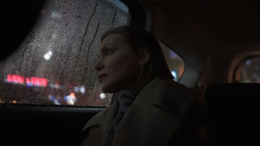Sad woman riding taxi in evening, looking into car window on rain, city lights Royalty-Free Stock Footage #1021901602