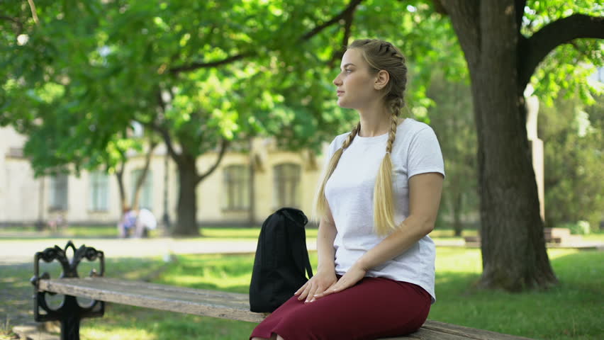 Young lady waiting for friend, sitting on bench walking away after nobody coming
