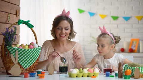 Little girl excitedly watching mother dipping egg in green food coloring, Easter