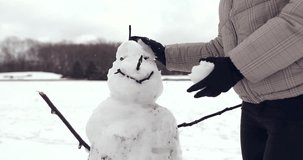 4K Footage of happy young girl standing on the street and sculpts a snowman, smile to camera. - Video