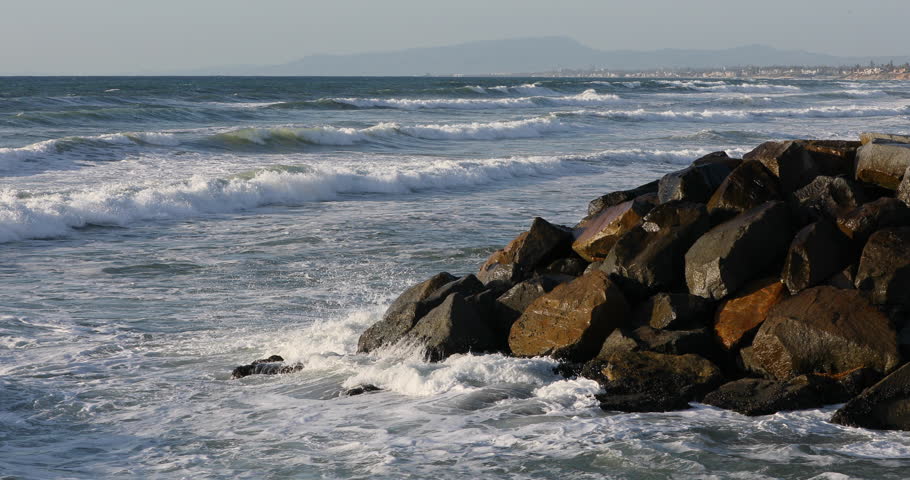 California ocean waves crash into rock coast. Beautiful southern California, Pacific Ocean beach. Waves and surf on sand and rocks. Summer vacation destination.