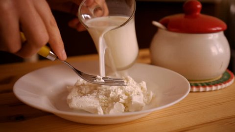A man pours milk into curds for dessert, on a wooden table. Cottage cheese on a plate. Slow Motion.
