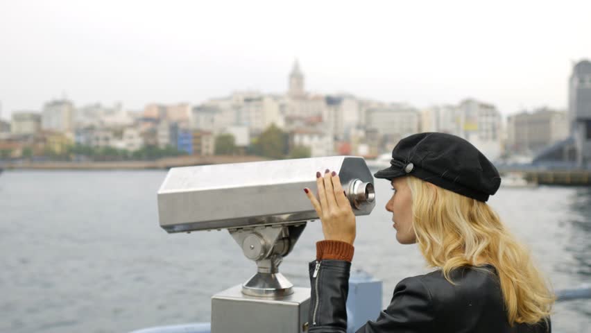 young woman looking through binoculars at Istanbul city standing on the shore