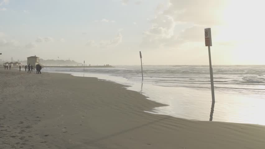 People walk on the beach of Tel Aviv during sunset in winter