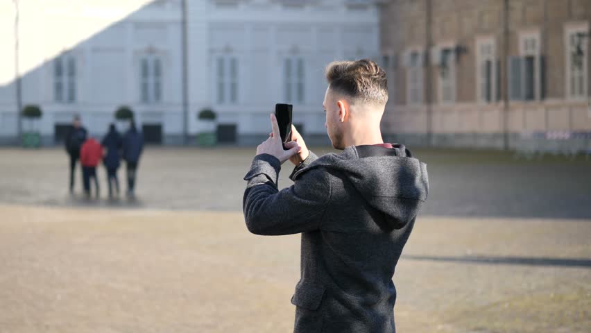 Young man taking photograph or filming video of historic place in European city with smartphone in a winter day